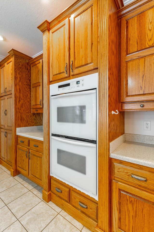 kitchen featuring light tile patterned floors, brown cabinets, light countertops, a textured ceiling, and double oven