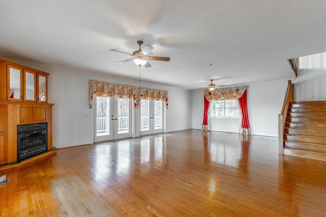 unfurnished living room with light wood-type flooring, french doors, a fireplace, and stairway