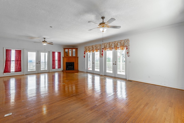 unfurnished living room featuring french doors, a fireplace, a ceiling fan, a textured ceiling, and wood finished floors