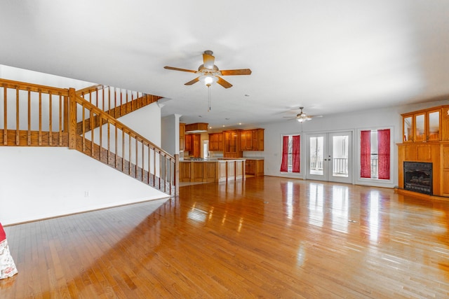 unfurnished living room featuring light wood-style floors, stairway, a fireplace with raised hearth, and french doors