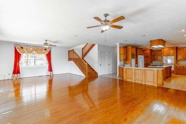 unfurnished living room featuring ceiling fan, stairway, and light wood-type flooring