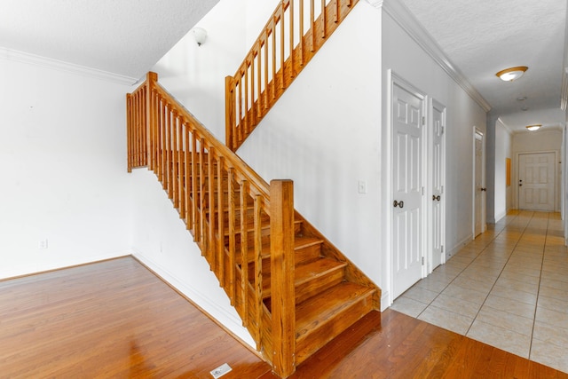 staircase with baseboards, a textured ceiling, ornamental molding, and wood finished floors