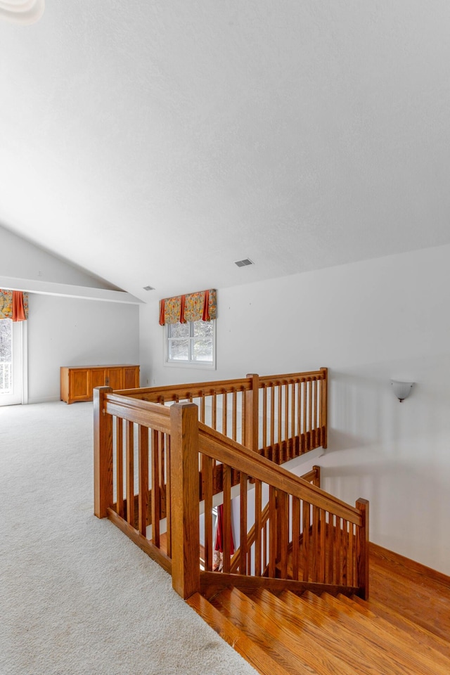 hall featuring lofted ceiling, carpet, visible vents, and an upstairs landing