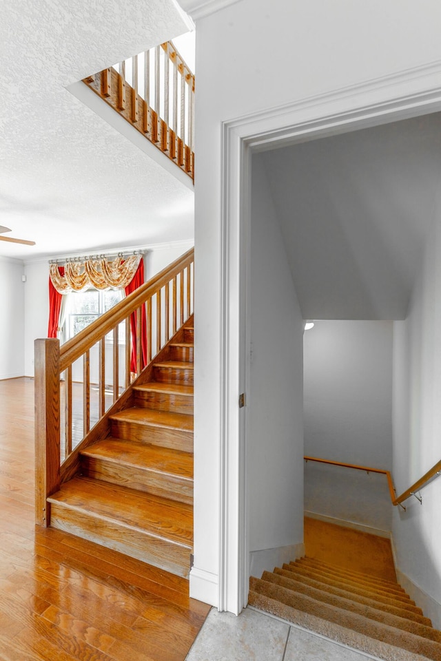 staircase with ceiling fan, a textured ceiling, and wood finished floors