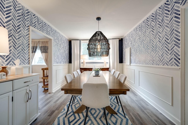 dining area with a wainscoted wall, wallpapered walls, an inviting chandelier, ornamental molding, and dark wood-type flooring