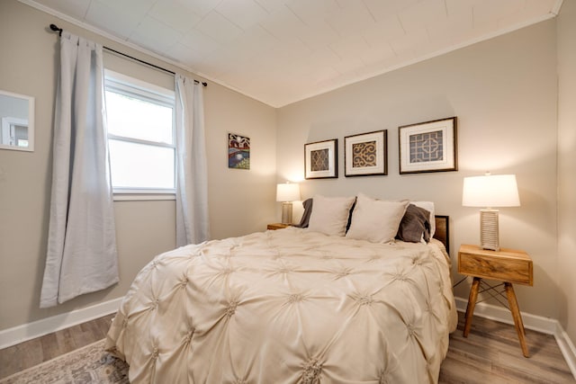 bedroom featuring baseboards, wood finished floors, and crown molding