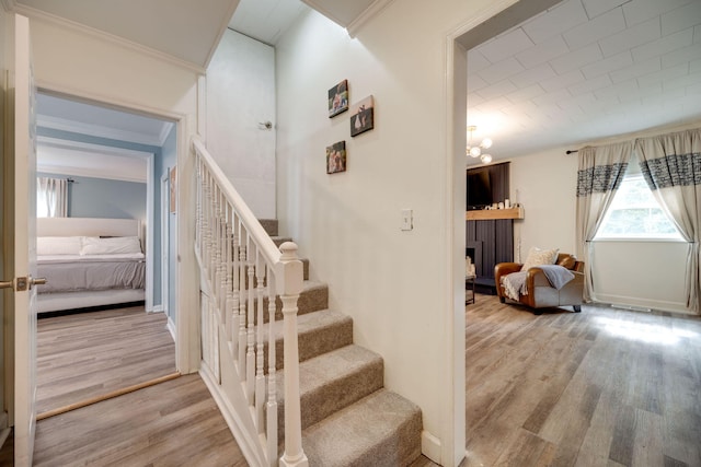 staircase with a fireplace, crown molding, wood finished floors, and baseboards