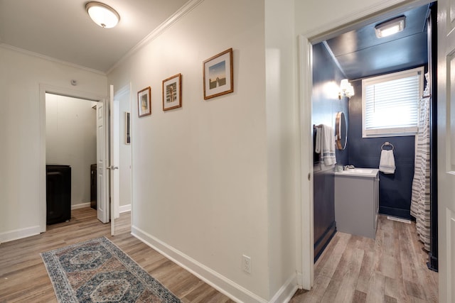 hallway with light wood-style floors, baseboards, and ornamental molding