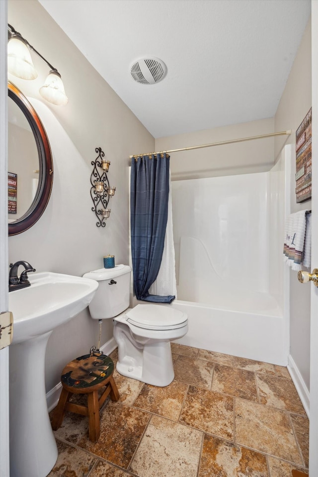 bathroom with stone tile floors, visible vents, shower / bathtub combination with curtain, toilet, and baseboards