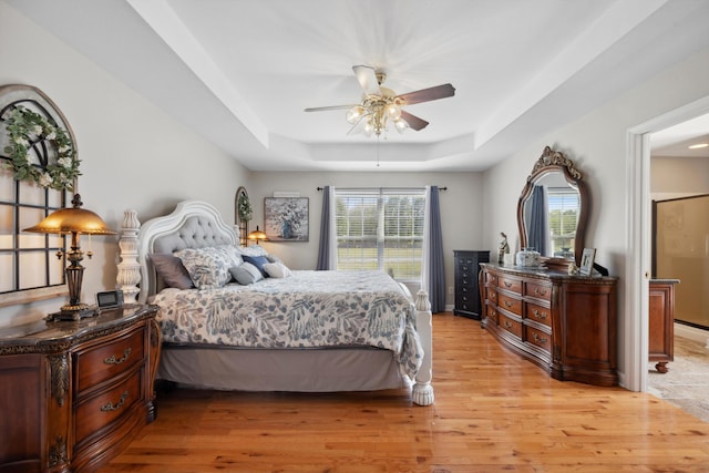 bedroom featuring ceiling fan, a tray ceiling, and light wood-type flooring