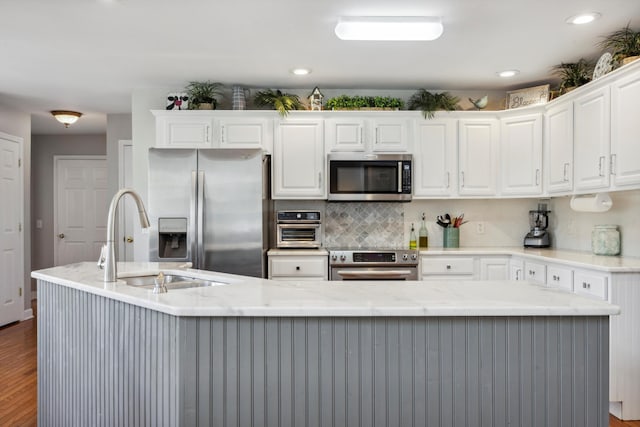 kitchen with stainless steel appliances, wood finished floors, a sink, white cabinetry, and decorative backsplash