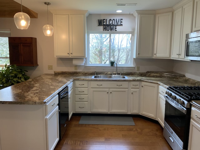 kitchen featuring dark wood finished floors, appliances with stainless steel finishes, white cabinetry, a sink, and a peninsula