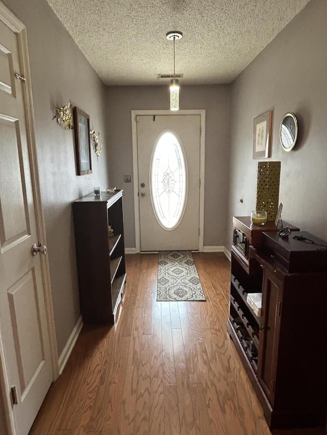 foyer entrance featuring visible vents, wood finished floors, baseboards, and a textured ceiling