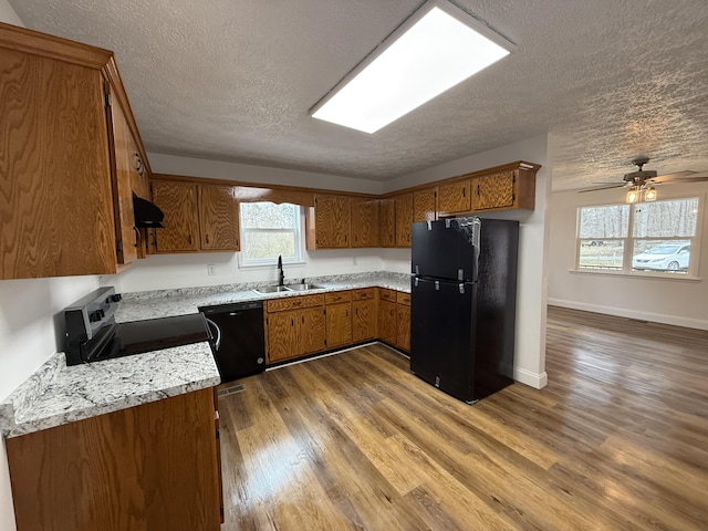 kitchen featuring brown cabinets, light countertops, a sink, wood finished floors, and black appliances