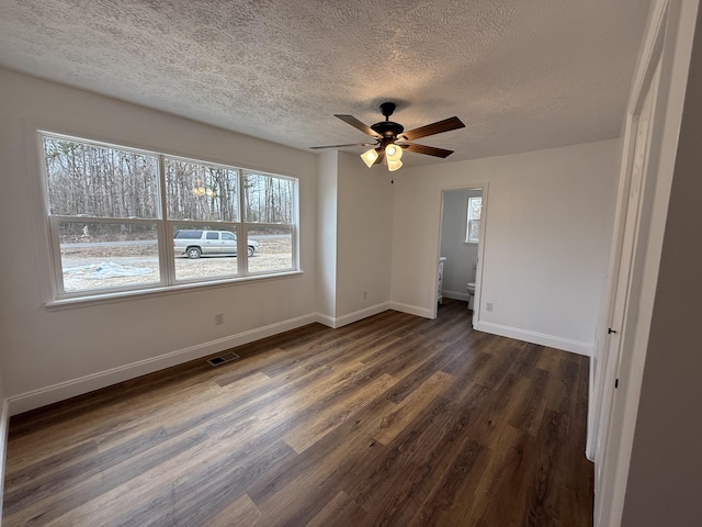 interior space with a textured ceiling, a ceiling fan, visible vents, baseboards, and dark wood-style floors