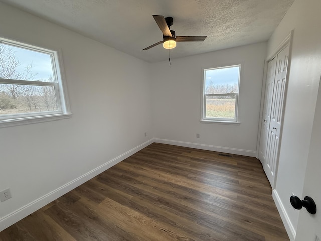 unfurnished bedroom featuring multiple windows, dark wood finished floors, and baseboards