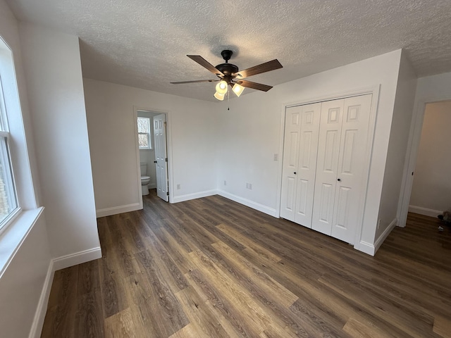 unfurnished bedroom featuring a textured ceiling, a closet, baseboards, and dark wood-style flooring