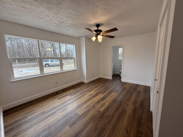 unfurnished bedroom featuring visible vents, a textured ceiling, baseboards, and dark wood-type flooring