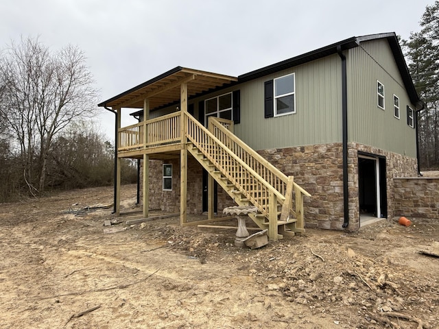 rear view of house featuring a deck, stone siding, stairway, and an attached garage