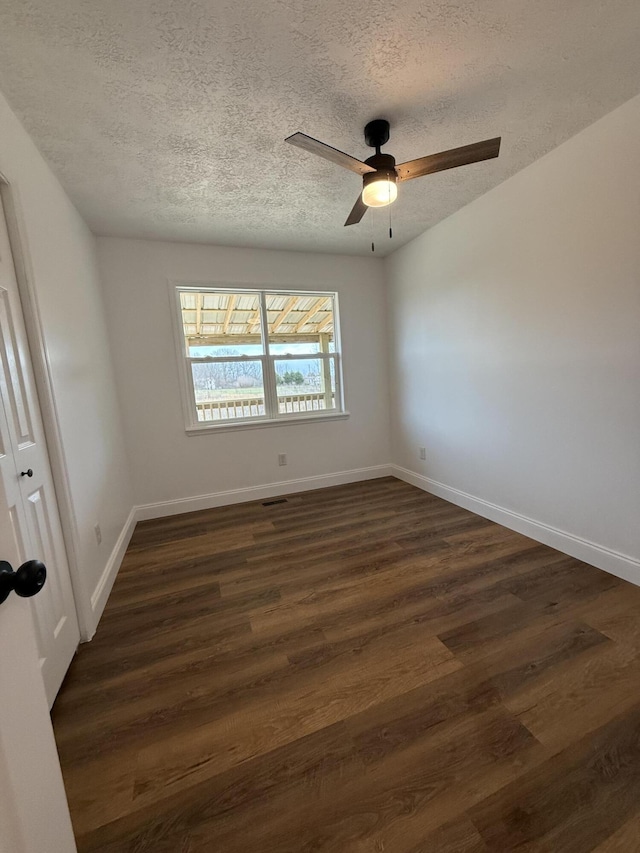 spare room featuring dark wood-type flooring, a textured ceiling, baseboards, and a ceiling fan