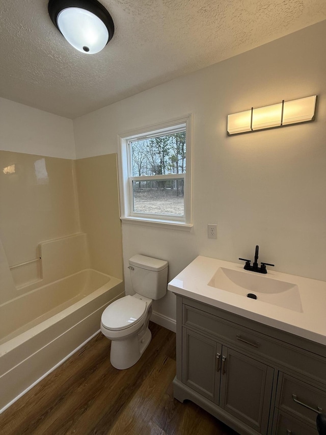 full bathroom with a textured ceiling, shower / tub combination, toilet, wood finished floors, and vanity