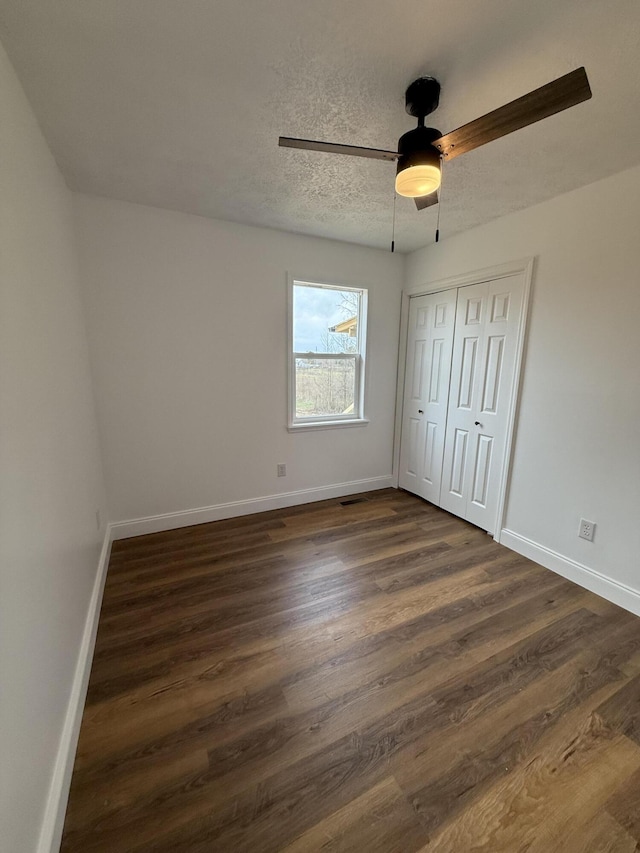 unfurnished bedroom with a textured ceiling, a ceiling fan, baseboards, a closet, and dark wood finished floors