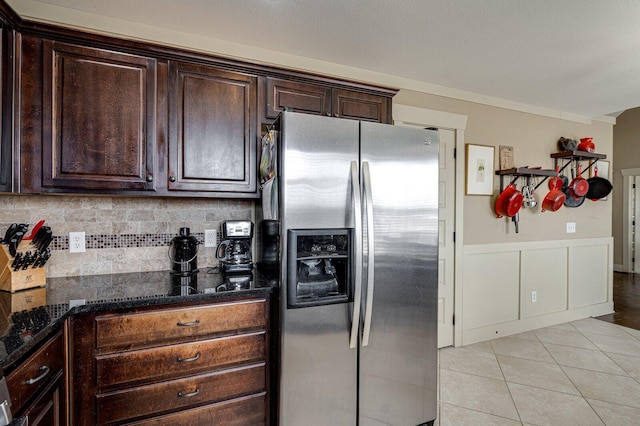 kitchen featuring dark brown cabinets, dark stone counters, light tile patterned floors, wainscoting, and stainless steel refrigerator with ice dispenser