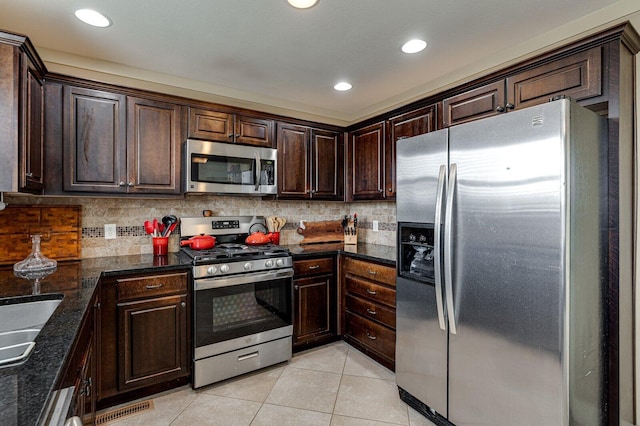 kitchen featuring dark stone countertops, light tile patterned floors, stainless steel appliances, decorative backsplash, and dark brown cabinets