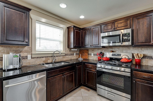 kitchen featuring tasteful backsplash, dark brown cabinets, light tile patterned floors, stainless steel appliances, and a sink