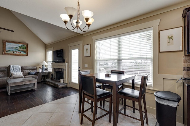 tiled dining room with a chandelier, a fireplace with raised hearth, and lofted ceiling