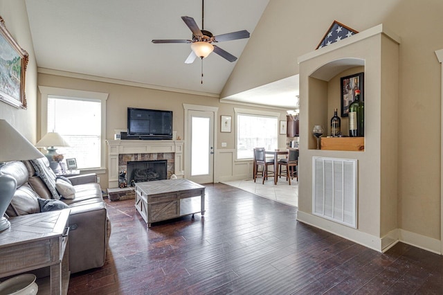 living area with visible vents, dark wood-type flooring, ceiling fan, a stone fireplace, and high vaulted ceiling