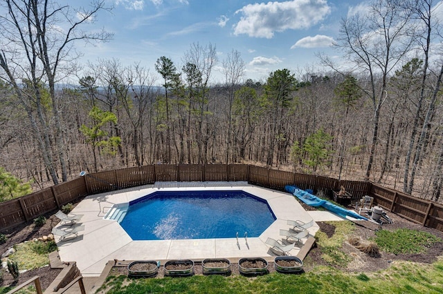 view of swimming pool with a patio area, a fenced in pool, a wooded view, and a fenced backyard