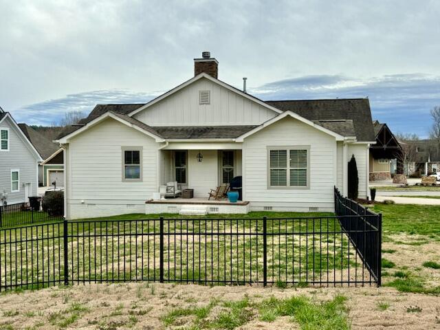 rear view of house with covered porch, a chimney, a fenced front yard, crawl space, and a lawn