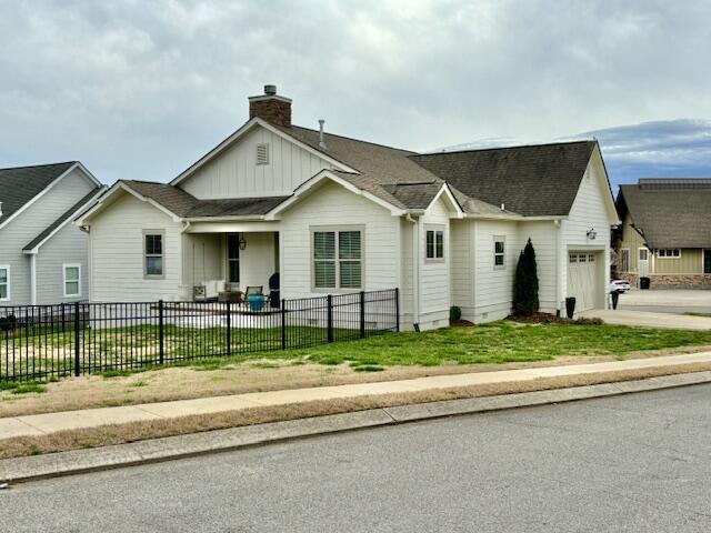 view of front facade featuring a fenced front yard, an attached garage, concrete driveway, and a chimney