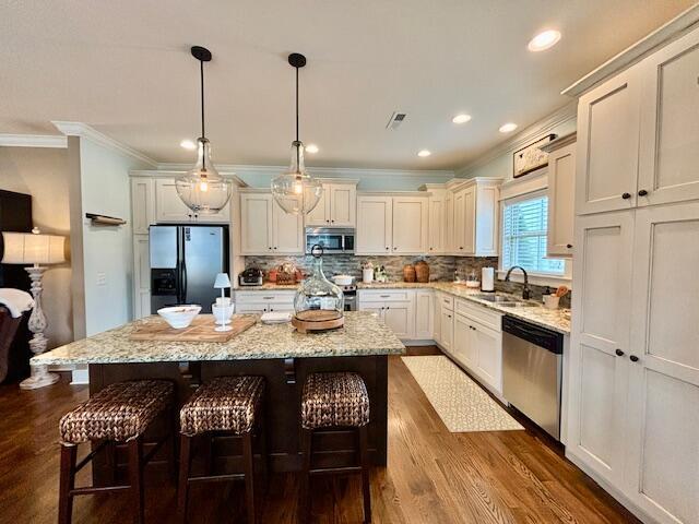 kitchen with a kitchen bar, visible vents, a sink, backsplash, and stainless steel appliances