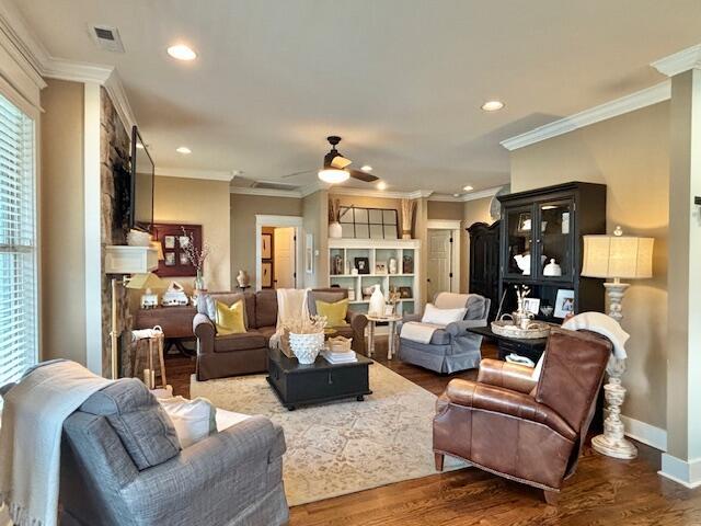 living room featuring visible vents, baseboards, wood finished floors, and crown molding