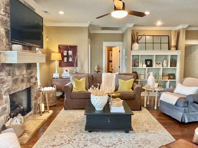 living room featuring visible vents, ceiling fan, ornamental molding, a fireplace, and wood finished floors