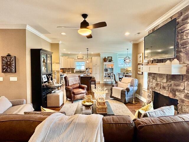 living area featuring baseboards, ceiling fan, ornamental molding, light wood-style flooring, and a fireplace