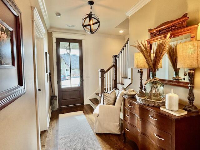 doorway to outside with dark wood finished floors, visible vents, ornamental molding, and stairs