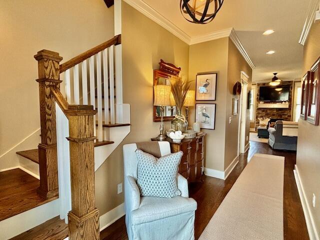 interior space featuring wood finished floors, a stone fireplace, crown molding, baseboards, and stairs