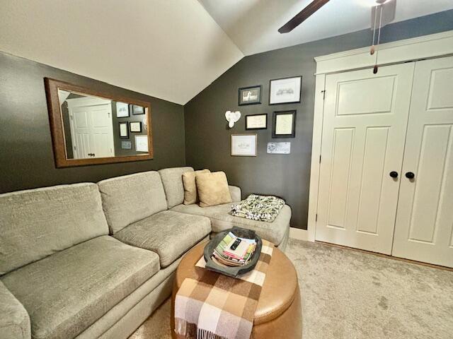 living area featuring vaulted ceiling, light colored carpet, and ceiling fan