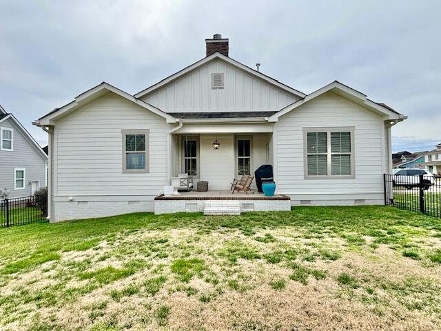 rear view of property featuring board and batten siding, fence, a lawn, a chimney, and crawl space