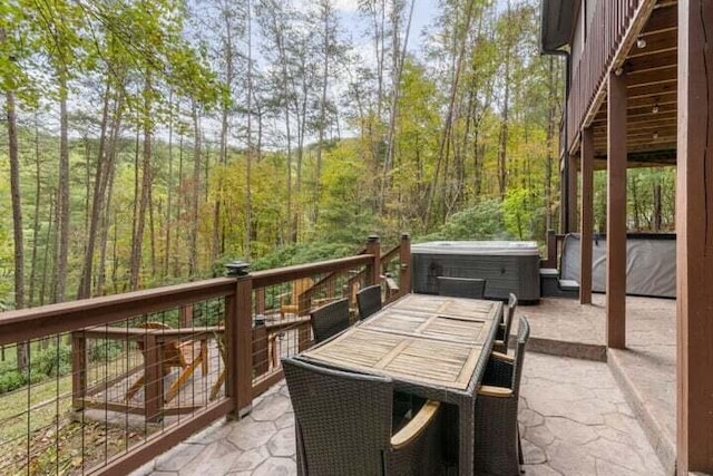 view of patio / terrace featuring outdoor dining space, a hot tub, and a view of trees