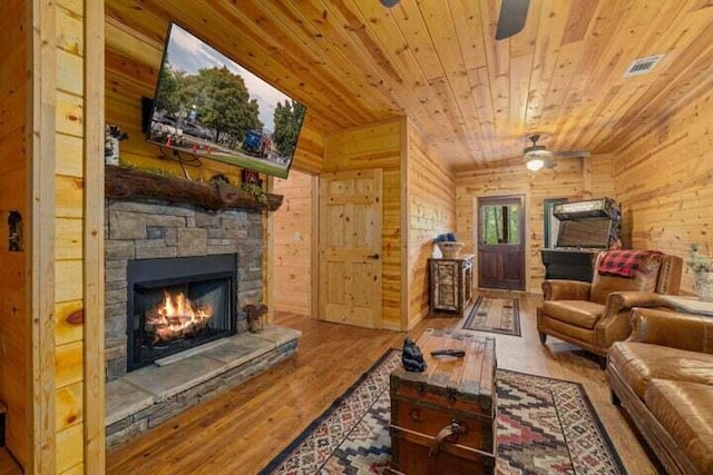 living room with a ceiling fan, wood finished floors, an outdoor stone fireplace, wooden ceiling, and wood walls