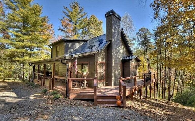 back of house featuring a chimney, a wooden deck, metal roof, and a standing seam roof