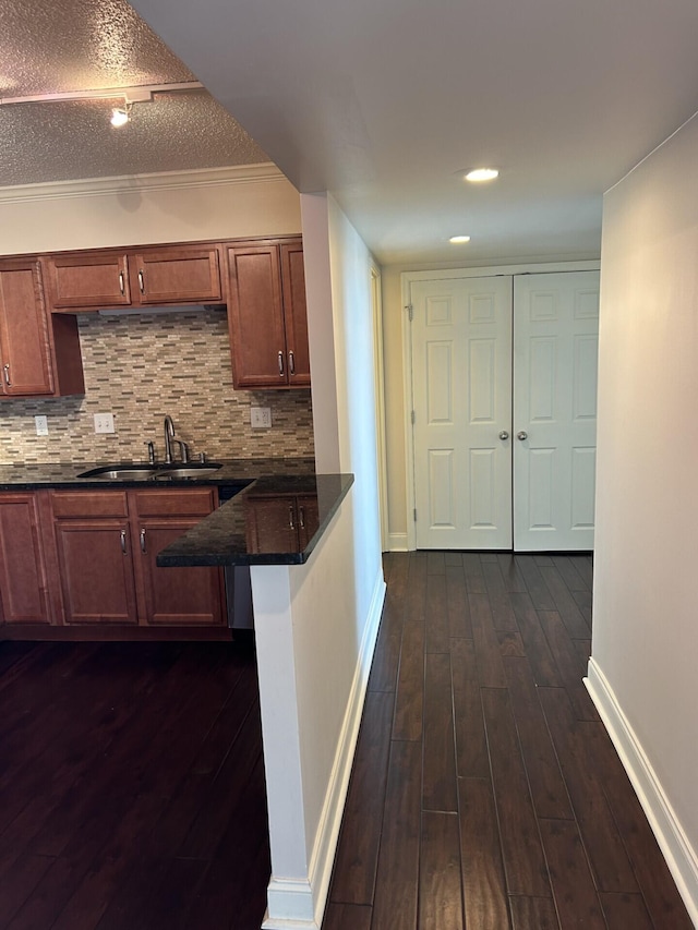 kitchen featuring dark countertops, tasteful backsplash, a sink, baseboards, and dark wood-style flooring