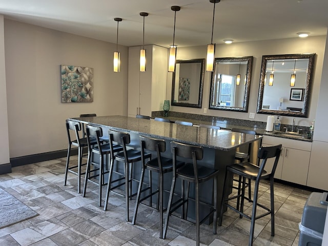 kitchen featuring baseboards, a kitchen island, a sink, a kitchen bar, and decorative light fixtures