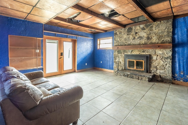 living area featuring french doors, a textured wall, tile patterned floors, a stone fireplace, and beam ceiling