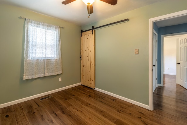 unfurnished room with a barn door, wood finished floors, baseboards, and visible vents