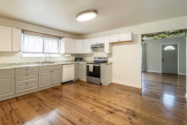 kitchen with baseboards, light wood finished floors, a sink, stainless steel appliances, and under cabinet range hood